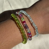 Peridot, night fever faceted sapphire, and faceted aquamarine bracelets stacked on a model's wrist.