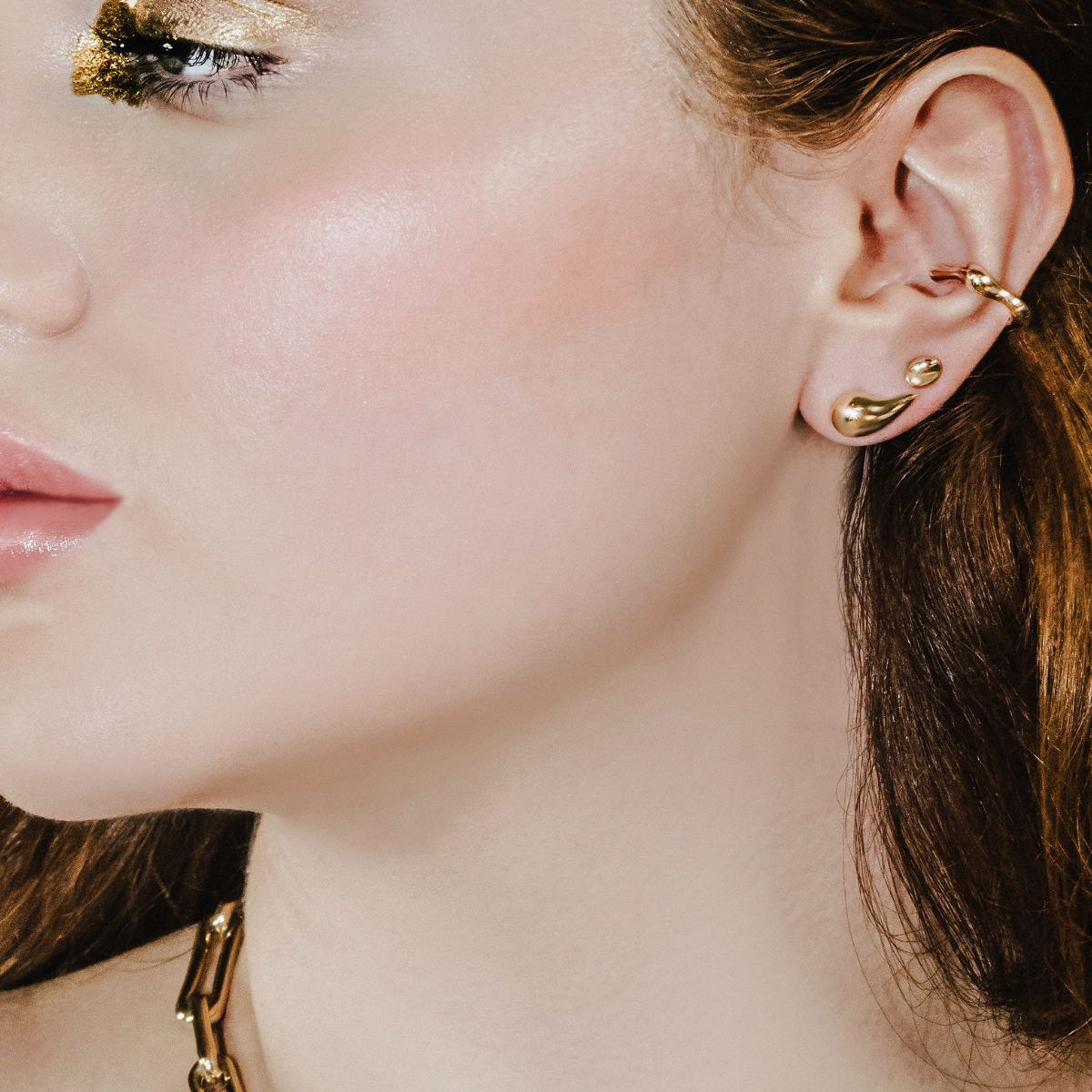 Molten ear cuff, stud, and small stud on the ear of a model with molten gold eye shadow.