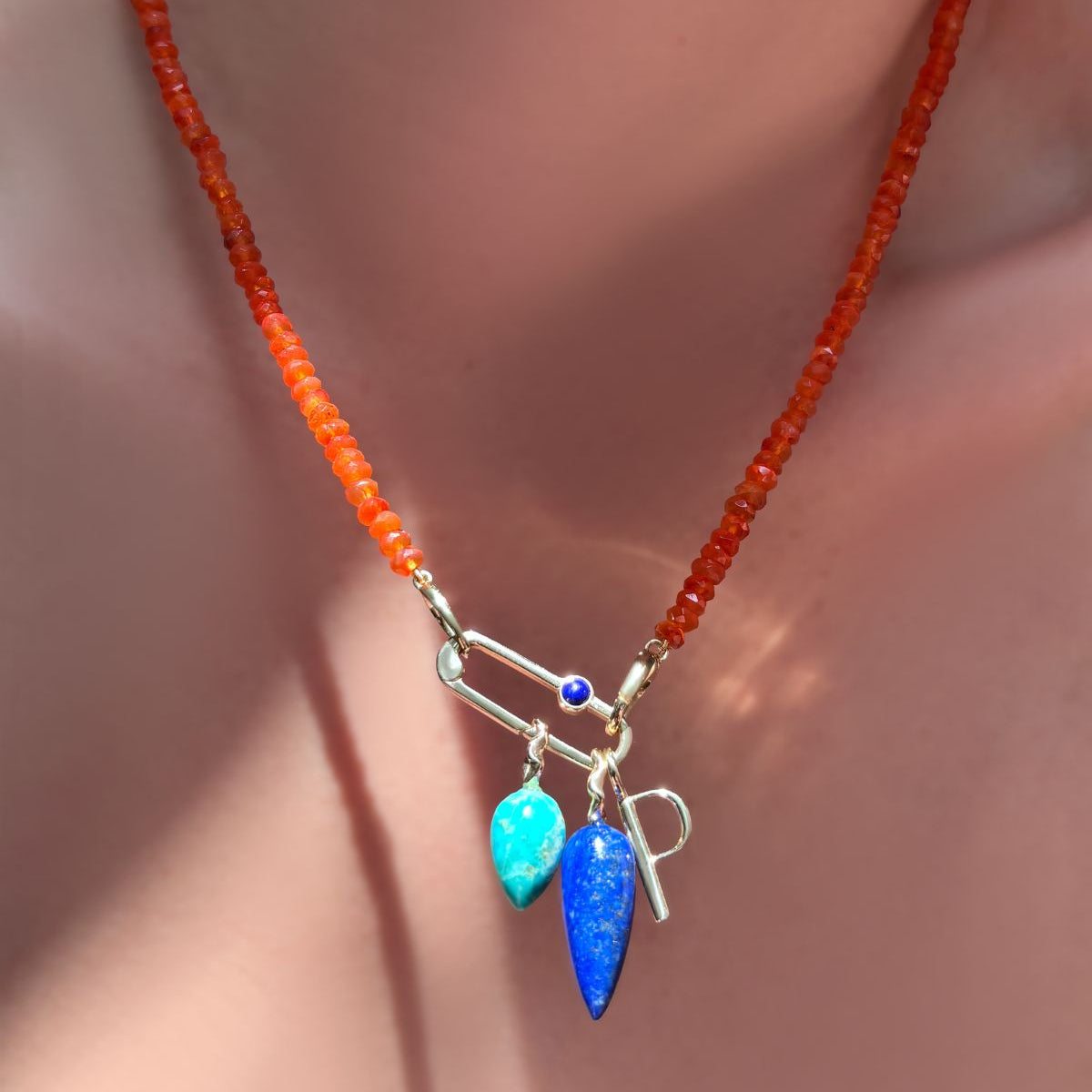 AMANDA PEARL faceted carnelian necklace holding a paperclip charm lock with lapis cabochon holding chrysocolla and lapis gemstone drop charms and letter P charm on a model's neck.