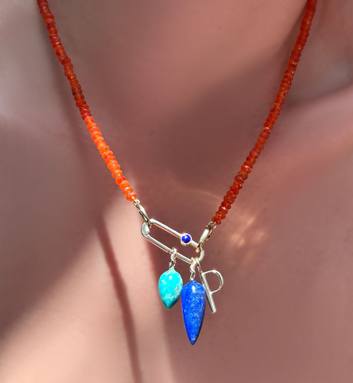 AMANDA PEARL faceted carnelian necklace holding a paperclip charm lock with lapis cabochon holding chrysocolla and lapis gemstone drop charms and letter P charm on a model's neck.