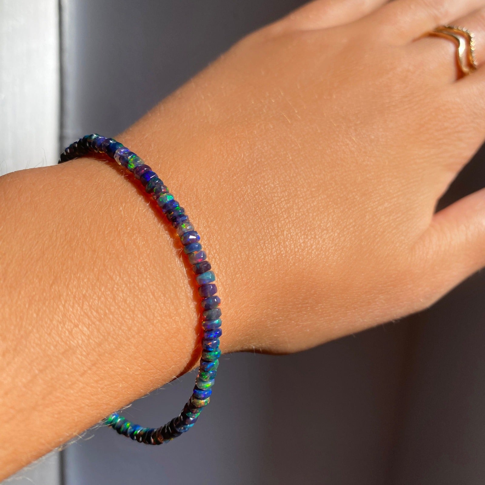 Shimmering beaded bracelet made of faceted opals in shades of black, blue, and green on a gold linking lobster clasp.