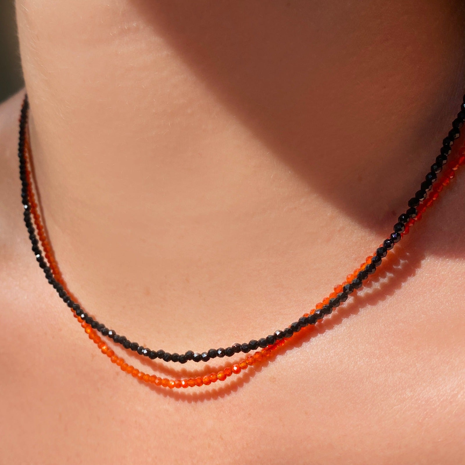 Two shimmering beaded necklaces made of 2mm faceted opals in shades of black and orange on a gold linking lobster clasp.