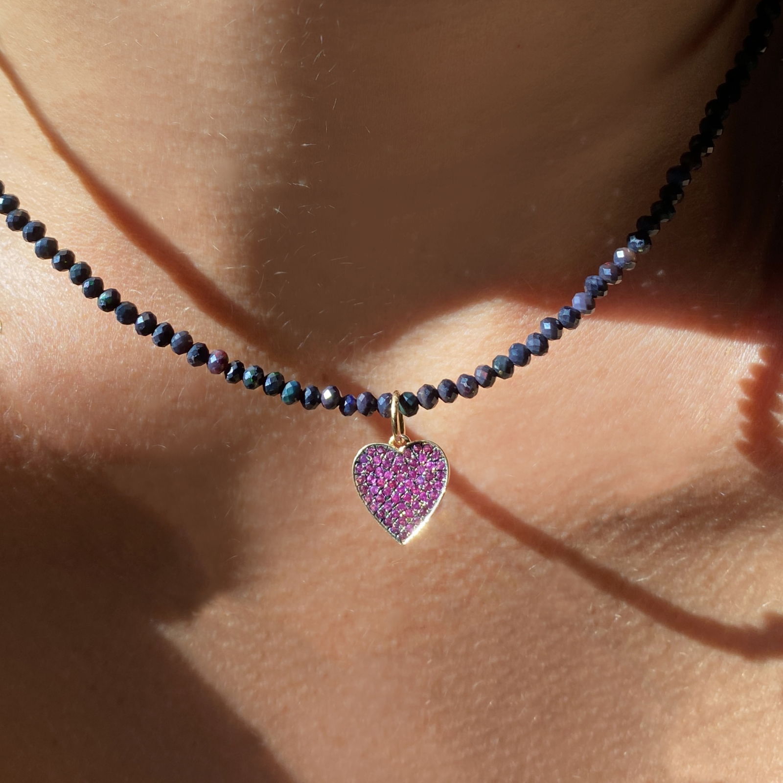 14k yellow gold medium pink stone pave blackened heart charm. Styled on a neck hanging from a beaded necklace.
