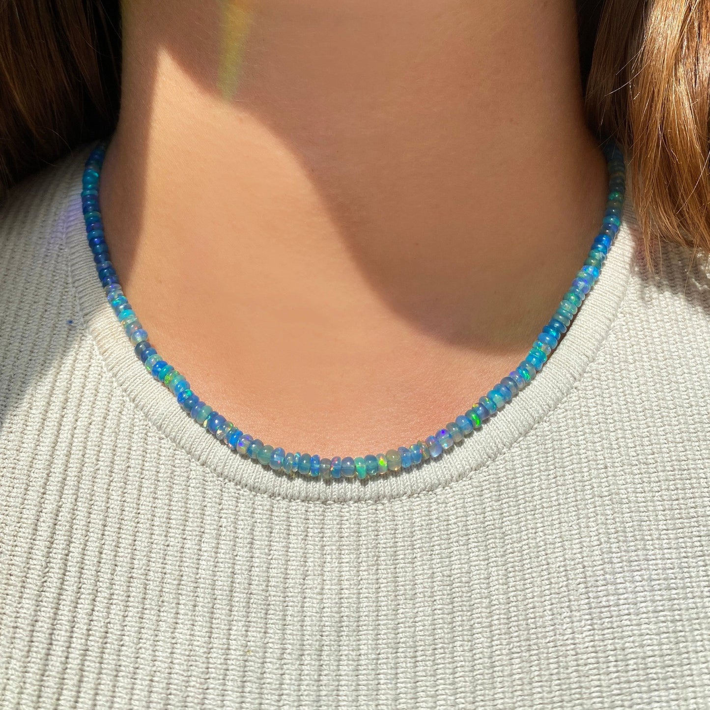 Shimmering beaded necklace made of smooth opal rondels in shades of blue, teal, and green on a slim gold oval clasp.