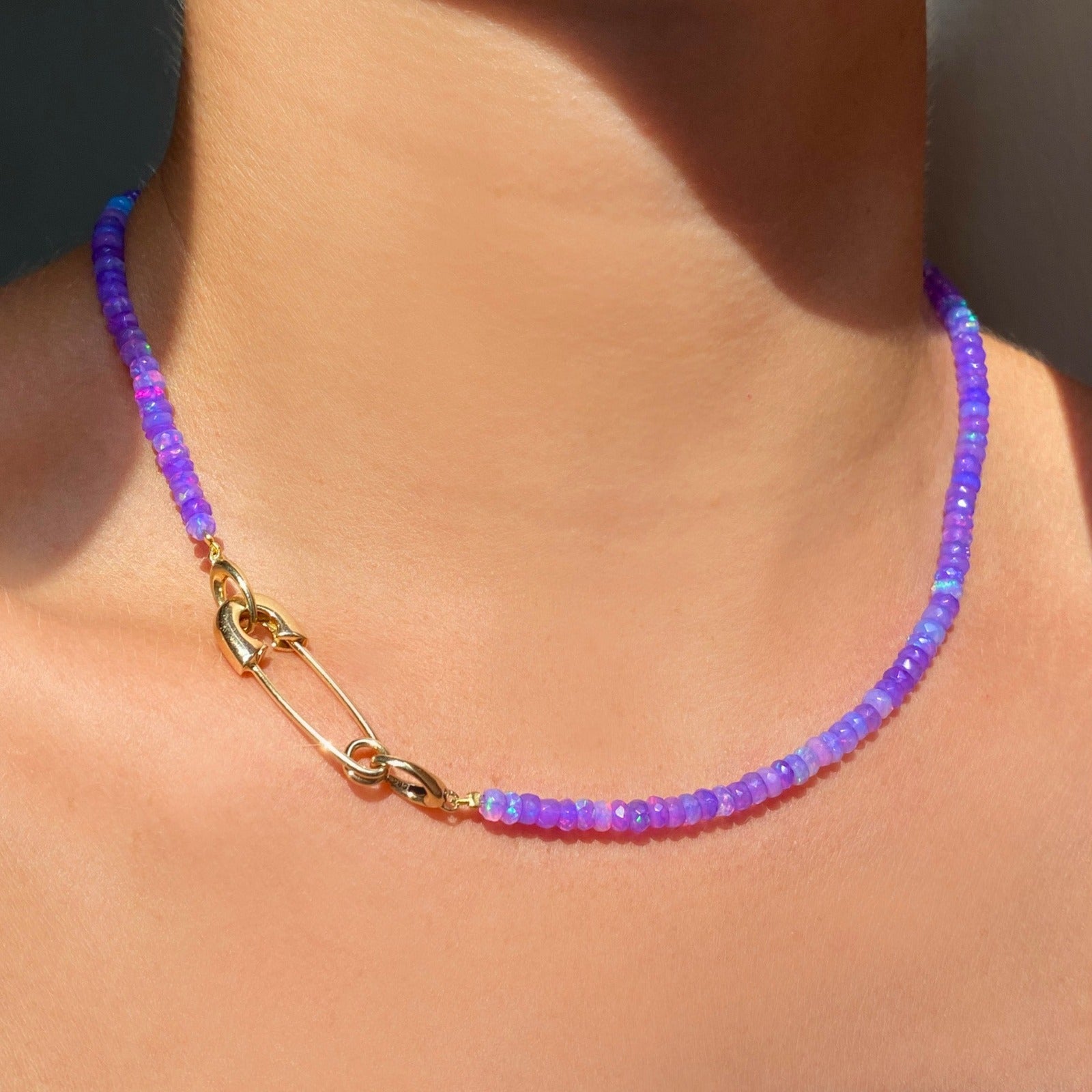 Shimmering beaded necklace made of faceted opals in shades of violet purple on a gold linking ovals clasp. Styled on a neck with a safety pin charm lock.