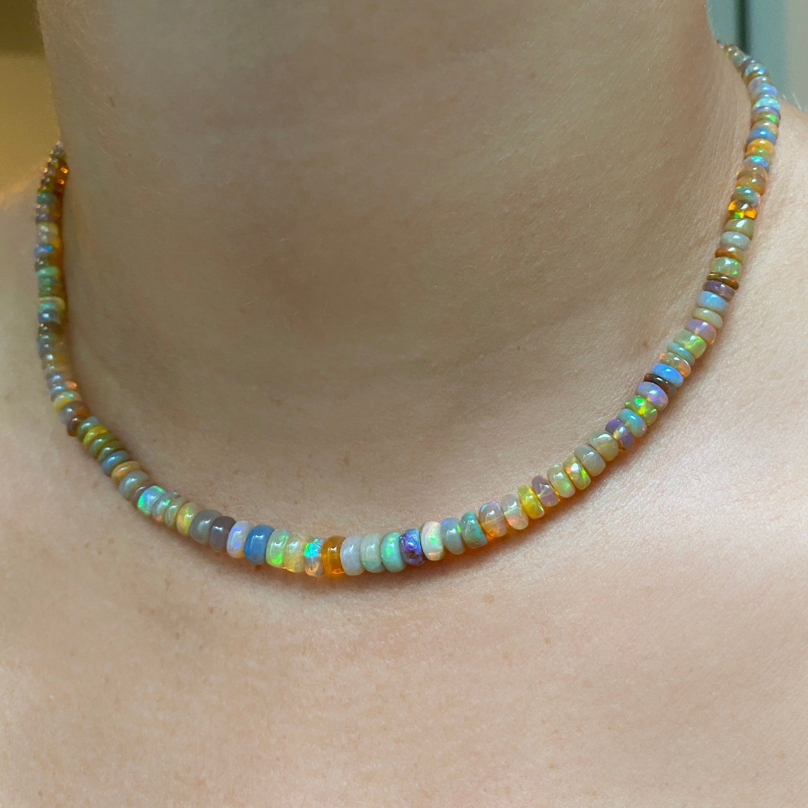 Shimmering beaded necklace made of smooth opal rondels in shades of light yellow, light orange, white, and brown on a slim gold lobster clasp.