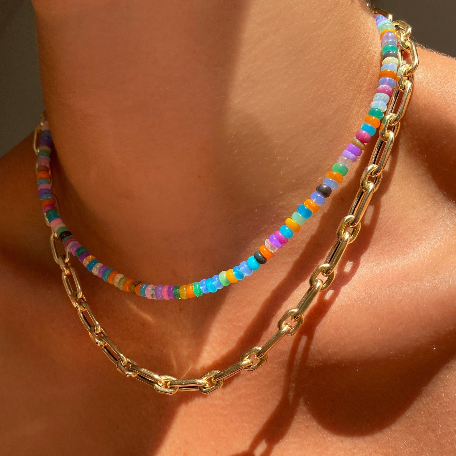 Shimmering beaded necklace made of smooth opal rondels in shades of fiery blues, hot pink, teal, and orange on a slim gold oval clasp. Styled on a neck layered with the diamond cut chain link necklace.