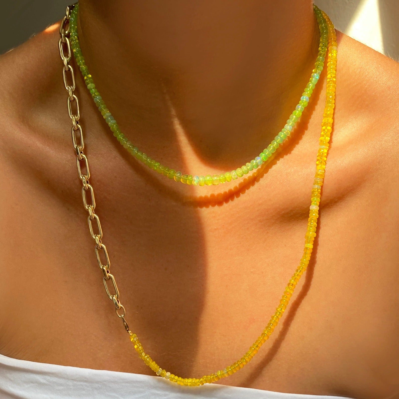 Shimmering beaded necklace made of smooth opal rondels in shades of yellow-green on a slim gold lobster clasp. Styled on a neck layered with the diamond cut link chain necklace.