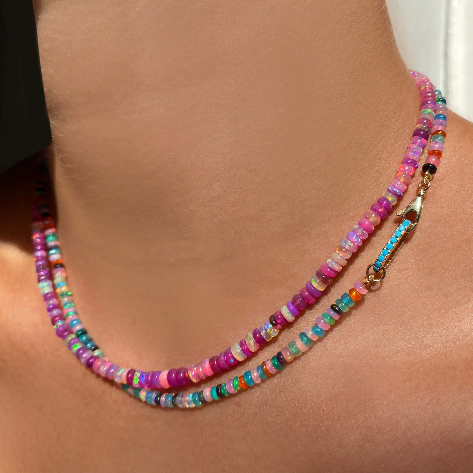 Shimmering beaded necklace made of smooth opal rondels in shades of teal, orange, purple and black on a slim gold lobster clasp. Styled on a neck layered with a fuchsia opal necklace