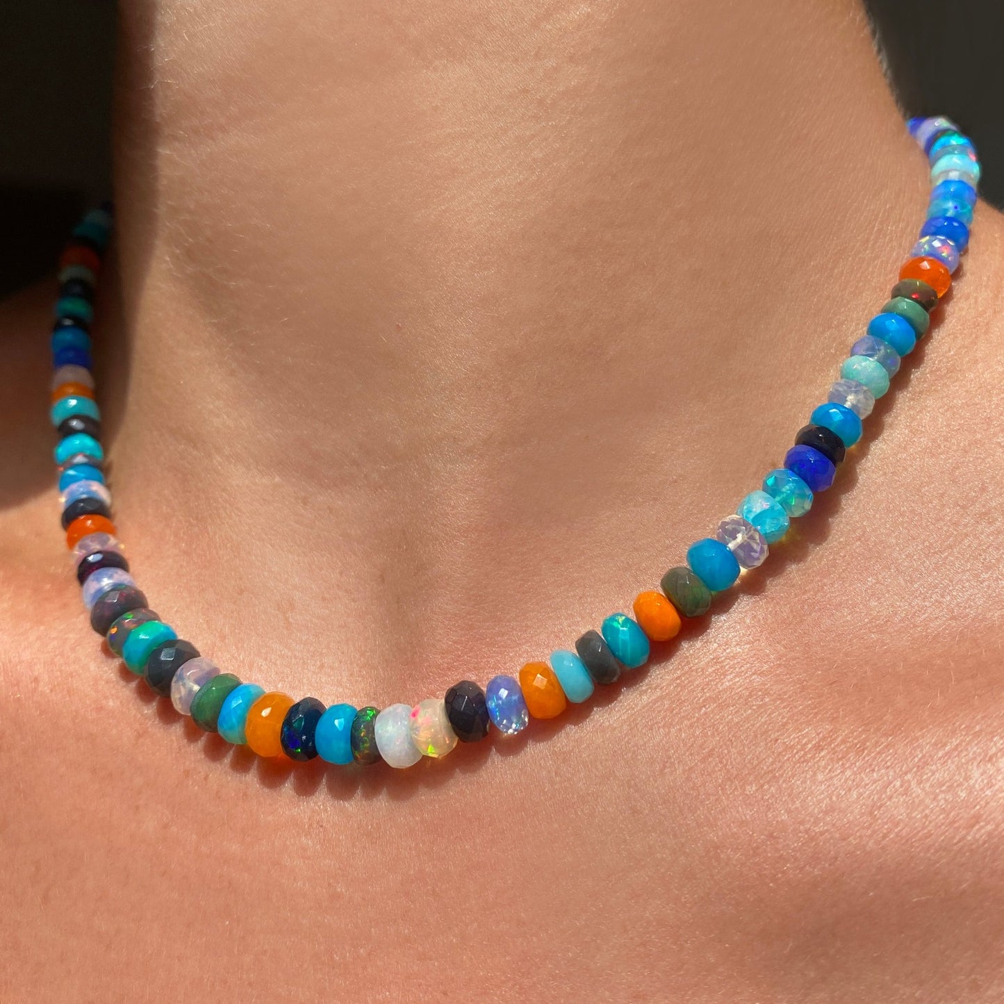 Shimmering beaded necklace made of faceted opals in shades of fiery blues, greens, teal, black, orange, and clear on a gold linking ovals clasp. 