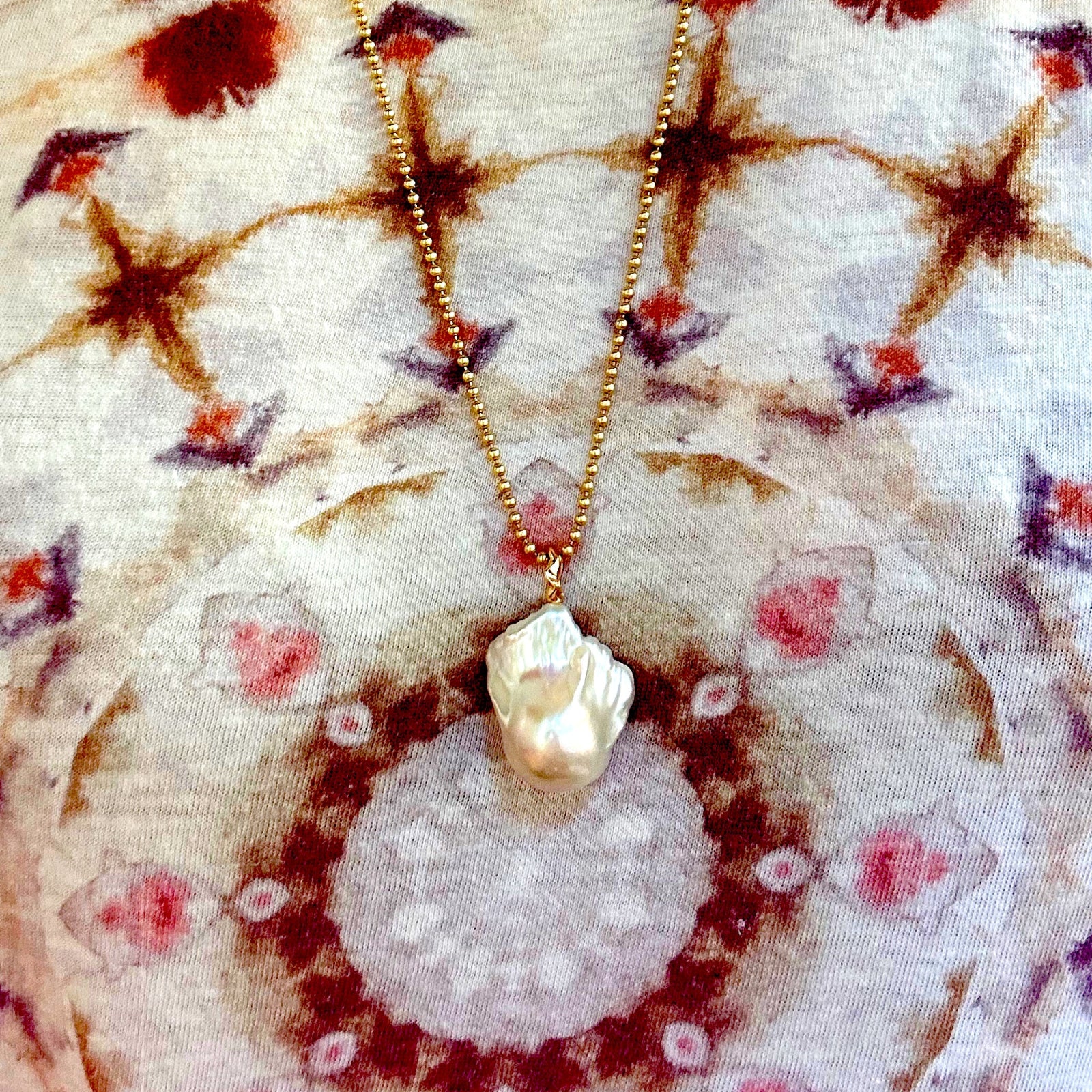 Baroque Pearl Charm with yellow gold ripple bale hanging from a 2mm bead chain over a tie dye tee.
