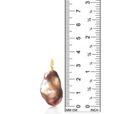 A pink peachy baroque pearl on a white background with a unique 14k yellow recycled gold ripple bale. It stands against a ruler for size comparison.