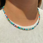 Shimmering beaded necklace made of smooth opal rondels in shades of teal, orange, purple and black on a slim gold lobster clasp. Styled on a neck