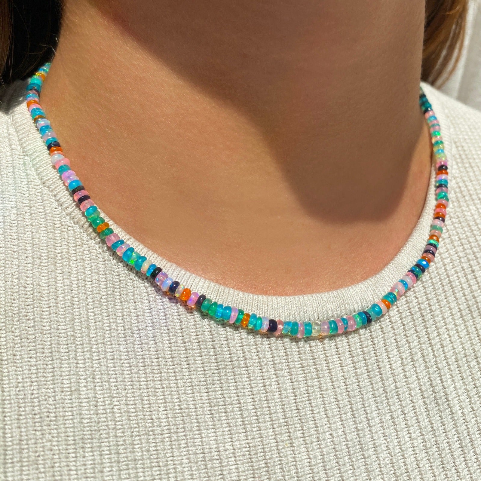 Shimmering beaded necklace made of smooth opal rondels in shades of teal, orange, purple and black on a slim gold lobster clasp. Styled on a neck