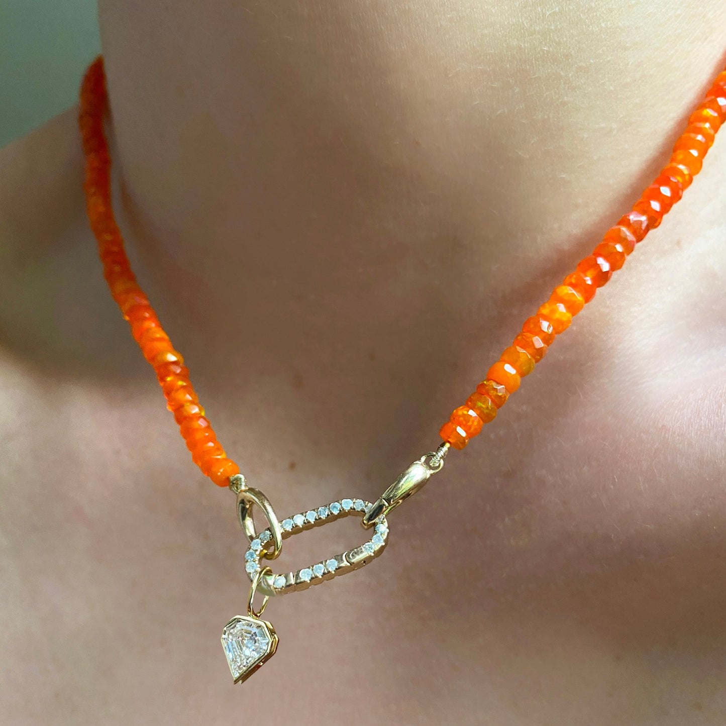 Shimmering beaded necklace made of faceted opals in shades of orange on a gold linking ovals clasp. Styled on a neck layered with a medium pave face charm lock and shield diamond solitaire charm. 