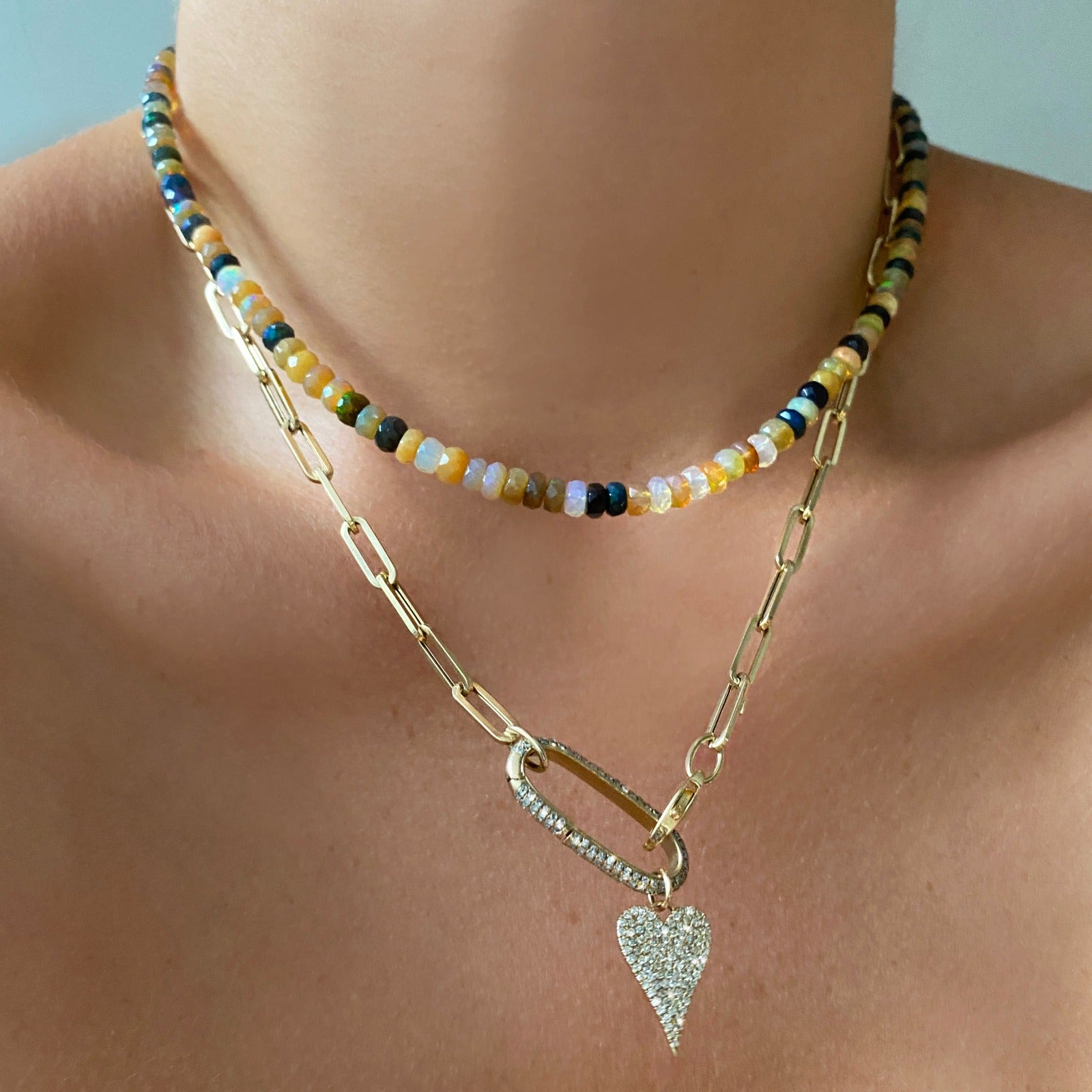 Shimmering beaded necklace made of faceted opals in shades of yellow, white, clear, brown, and black on a gold linking ovals clasp. Styled on a neck layered with the paperclip chain necklace, pave oval charm lock, and medium pave diamond heart.