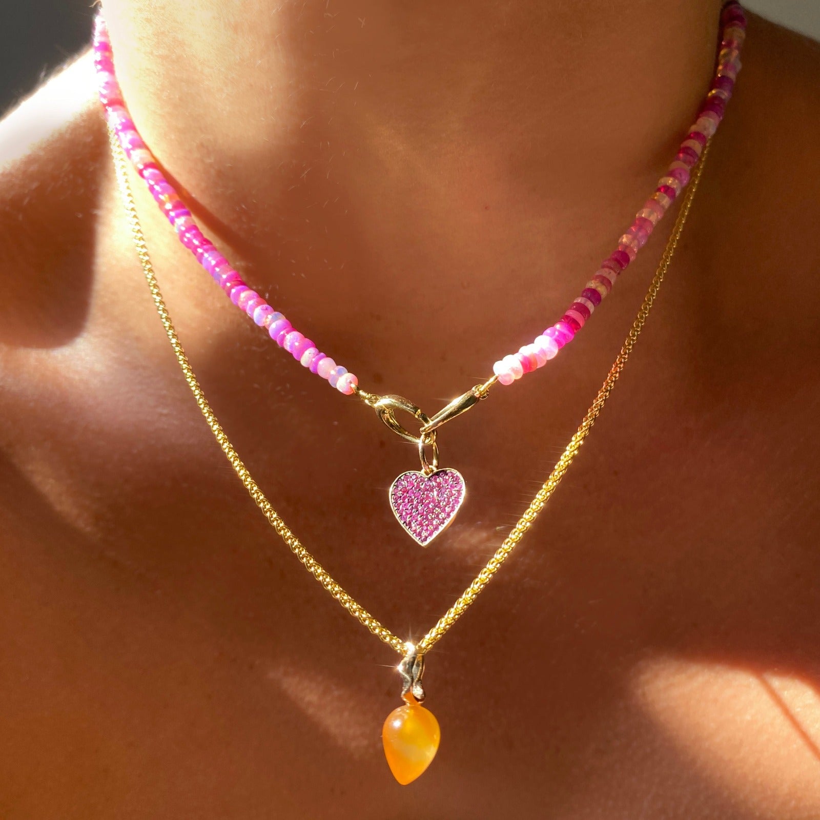 14k yellow gold medium pink stone pave blackened heart charm. Styled on a neck hanging from oval clasps of a beaded necklace. 