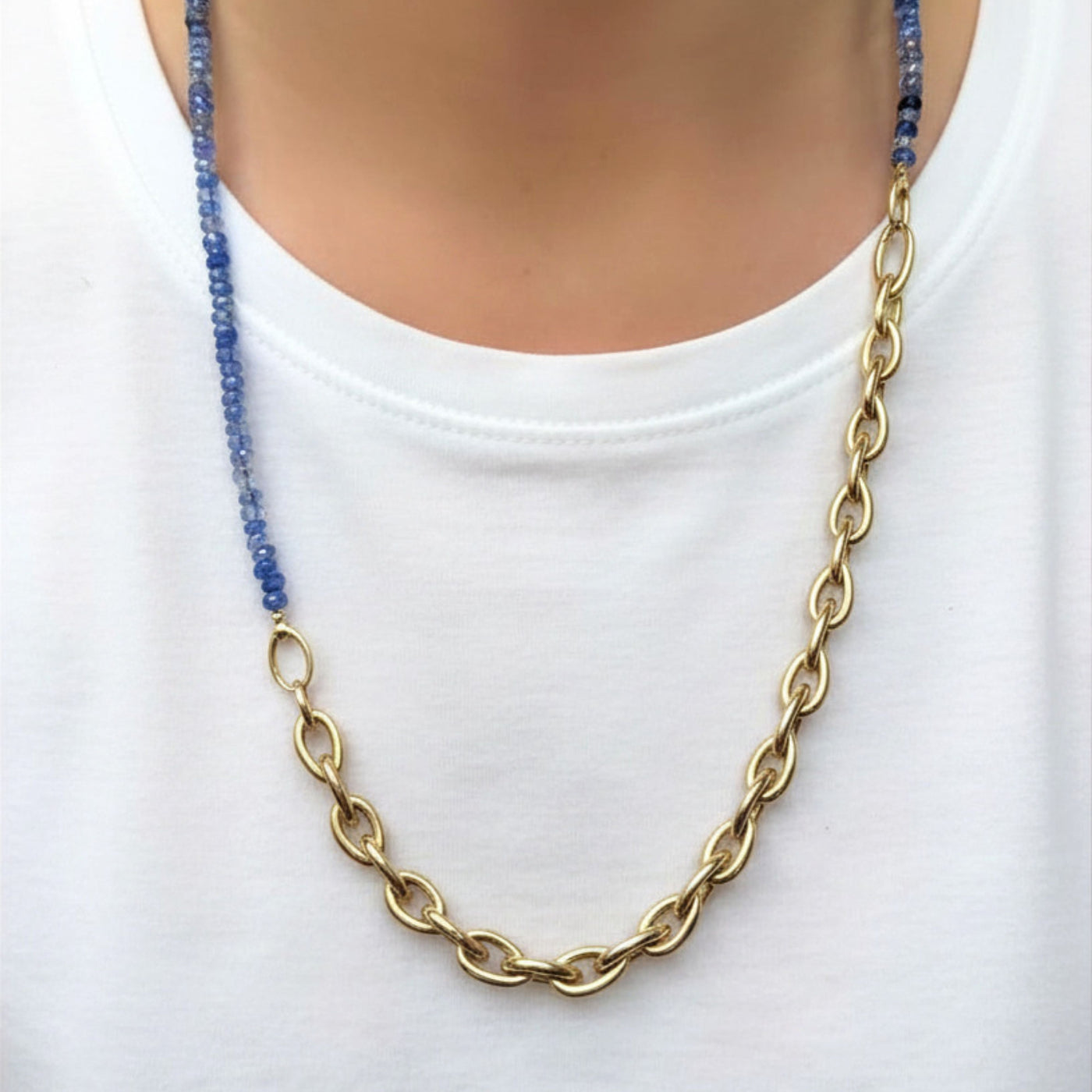 A woman in a plain white t-shirt shows how you can use your AMANDA PEARL evolution clasp to attach a denim sapphire necklace to a drop link bracelet to make one long, two tone necklace.