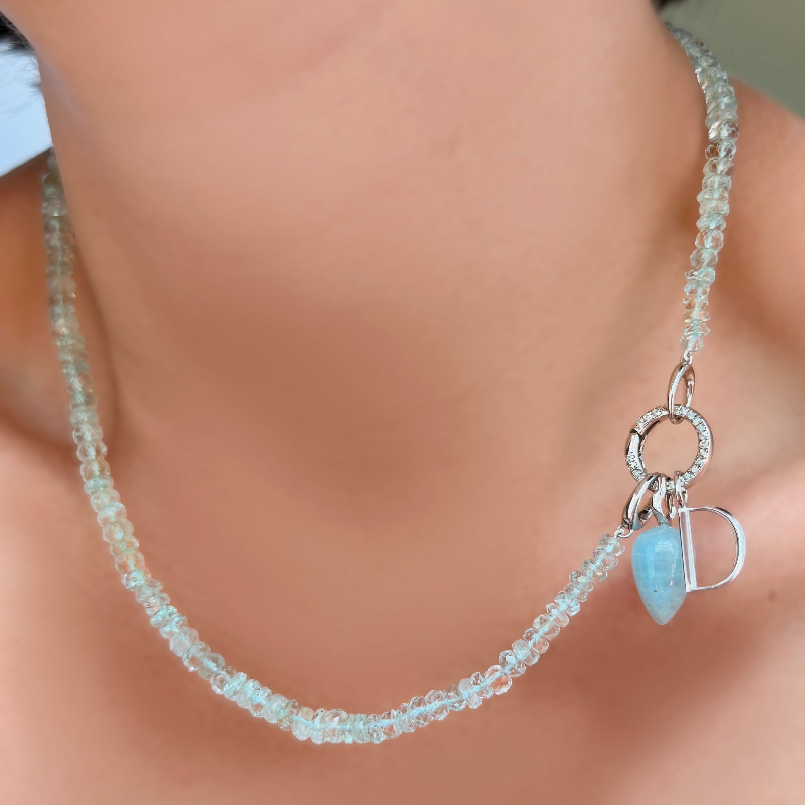 AMANDA PEARL Faceted Aquamarine Necklace with white gold evolution clasp holding a round pavé face charm lock with aquamarine drop charm and letter D charm on a model's neck.
