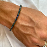 Shimmering beaded bracelet made of faceted opals in shades of black, blue, and green on a gold linking lobster clasp.