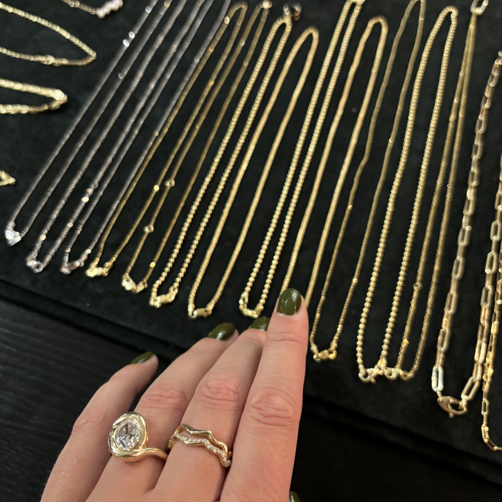 A close up of a hand shopping for chains in store at the AMANDA PEARL studio located in the hear of NYC. The hand wears AP rings cast in 14K yellow gold and featuring lab grown diamonds. 