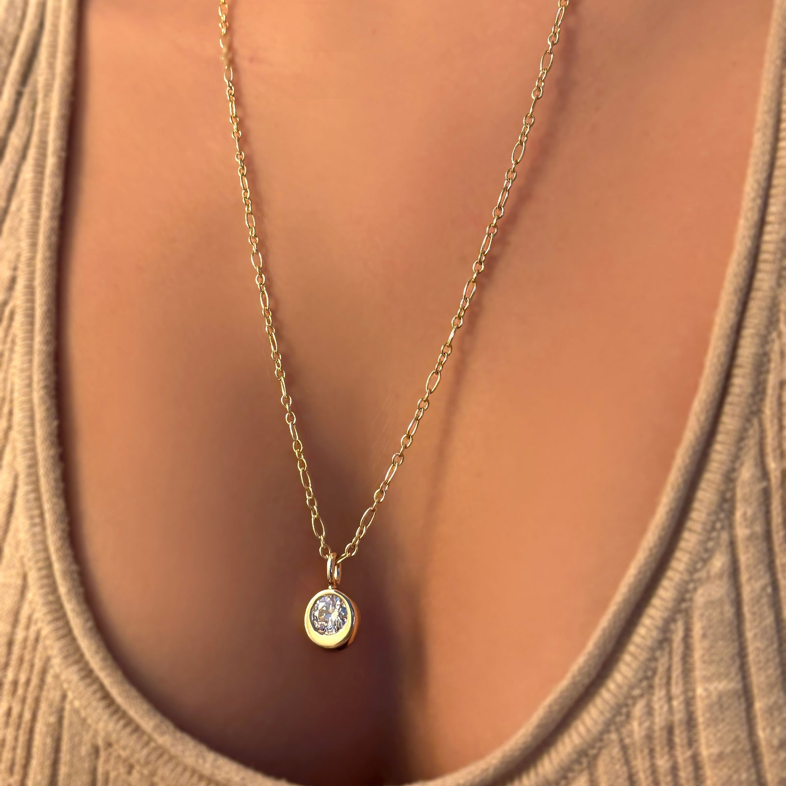 Irregular cable chain necklace with molten solitaire charm with white diamond set in recycled 14k yellow gold on a model's neck, paired with a beige knit.