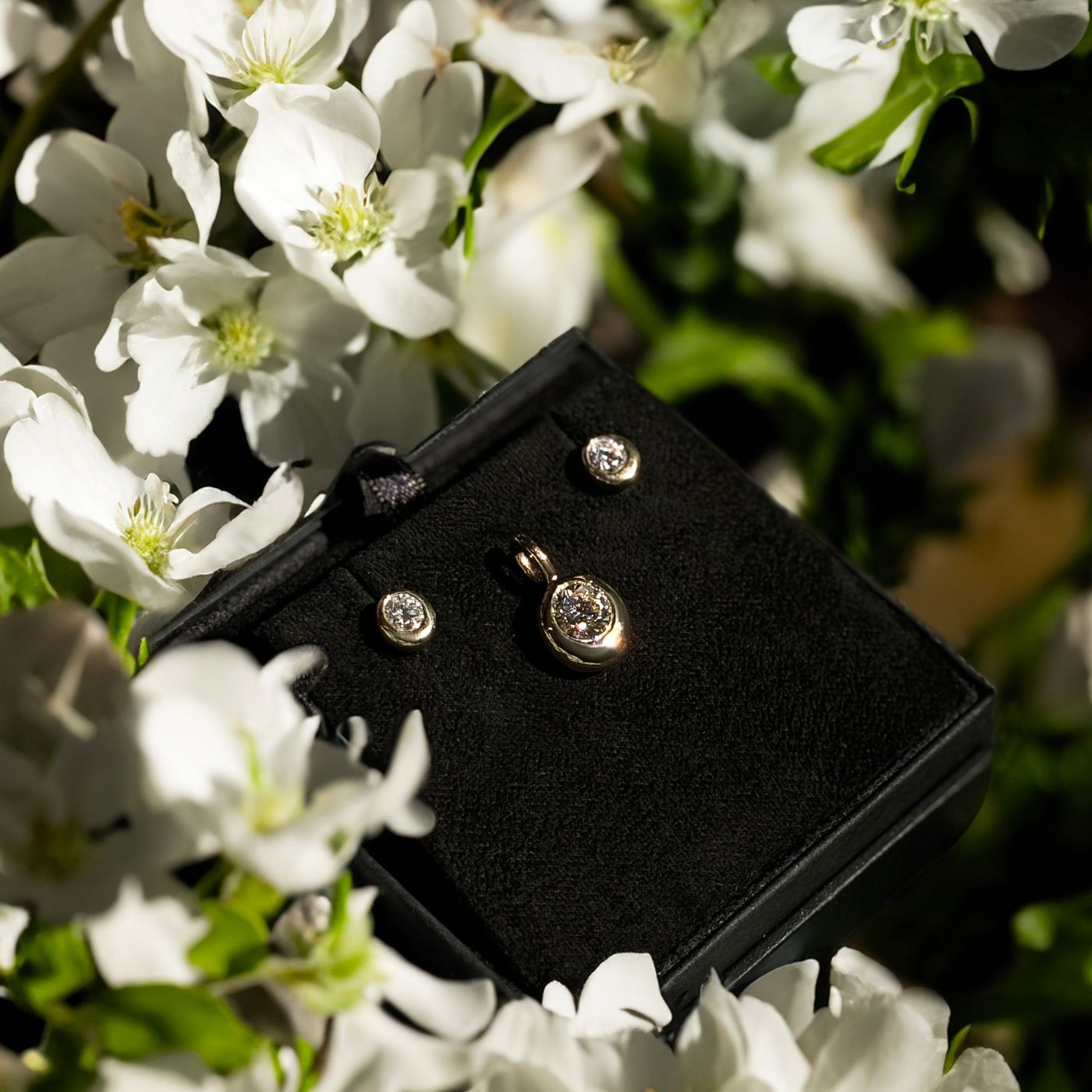 Mother's Day gift of Molten Solitaire Charm with matching stud earrings, surrounded by white cherry blossoms.
