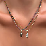 A single multi tourmaline necklace. with pyrite drop charm on recycled gold ripple bale layered over a 3mm bead chain with molten solitaire charm with pear-shaped diamond on a model's neck.