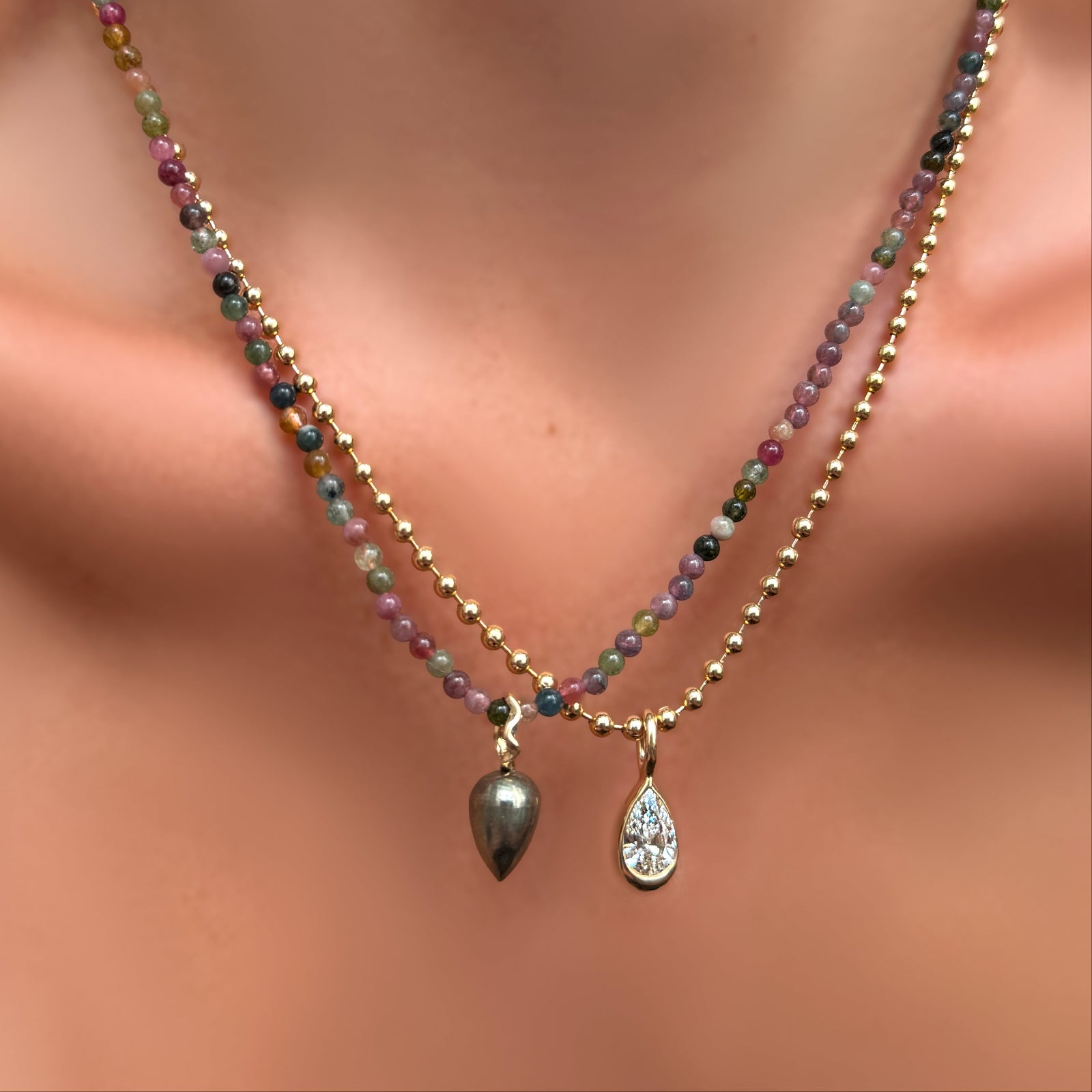 A single multi tourmaline necklace. with pyrite drop charm on recycled gold ripple bale layered over a 3mm bead chain with molten solitaire charm with pear-shaped diamond on a model's neck.