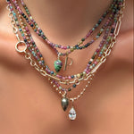 Layered muti tourmaline necklaces with gemstone drop charms, a molten solitaire pear shaped charm, and letter P charm over an irregular cable chain on a model's neck.