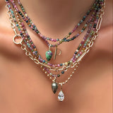Layered muti tourmaline necklaces with gemstone drop charms, a molten solitaire pear shaped charm, and letter P charm over an irregular cable chain on a model's neck.