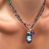 A single multi tourmaline necklace with a storm baroque pearl charm and amethyst drop charm on a model's neck under another strand of multi tourmalines.