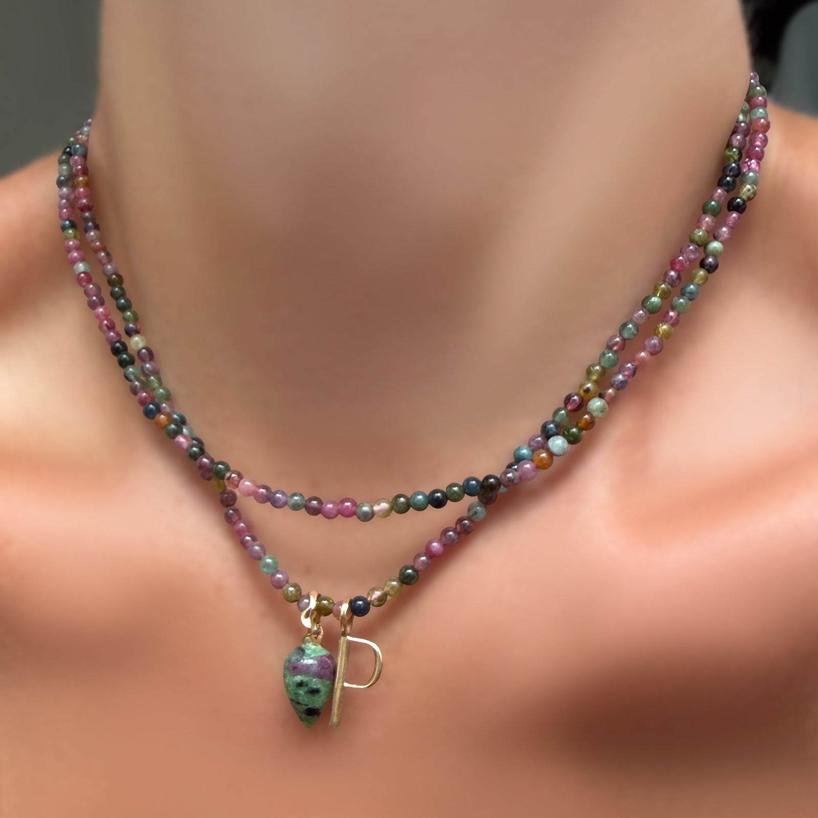 Two multi tourmaline necklaces on a model's neck, one with a ruby zoisite drop charm and letter P charm in recycled yellow gold..