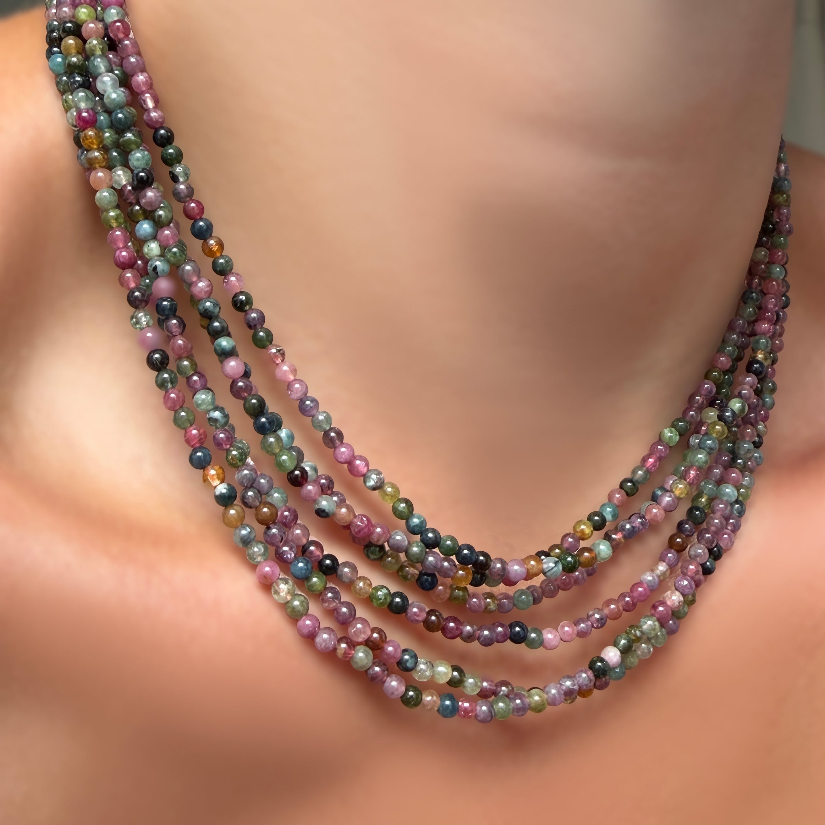 Multiple multi tourmaline necklaces layered on a model's neck.