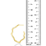 A photo of an undulating hoop earring next to a ruler showing that is is 3.3cm in height. It is made of 14k yellow gold with a rippling shape that is a play on a classic gold hoop earring.