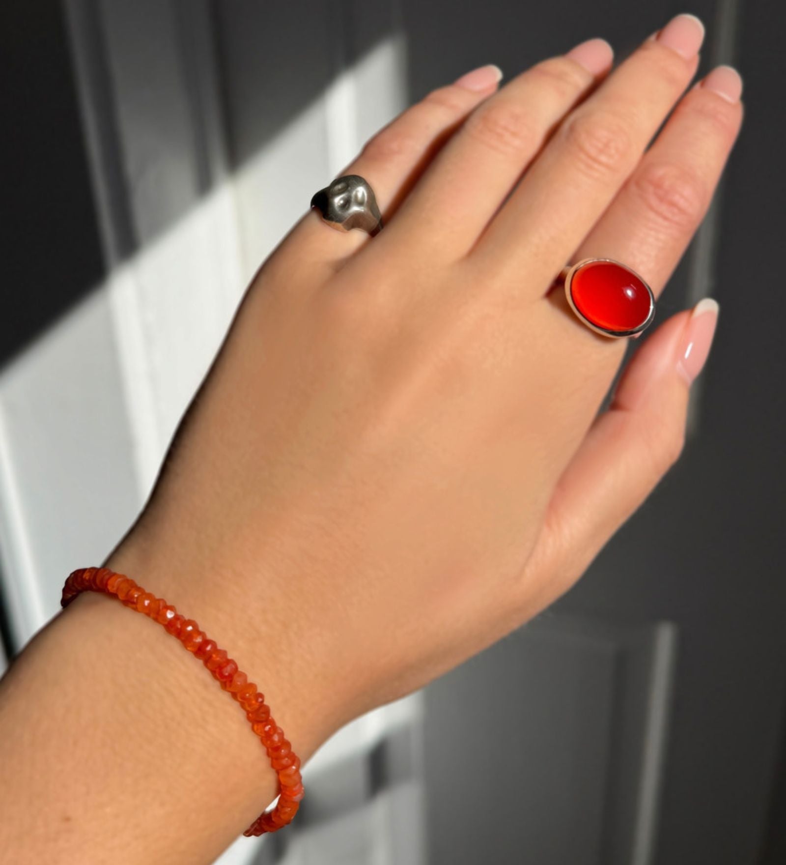 A model wearing an AMANDA PEARL faceted carnelian beaded bracelet along with a recycled sterling silver molten skull pinky ring and pebble ring with carnelian cabochon.