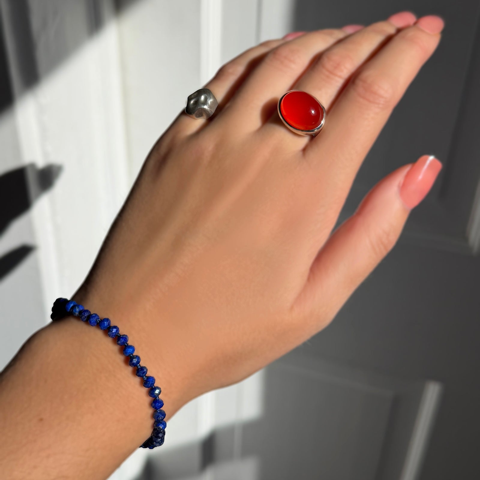 A model wearing an AMANDA PEARL faceted lapis beaded bracelet along with a recycled sterling silver molten skull pinky ring and molten pebble ring with carnelian.