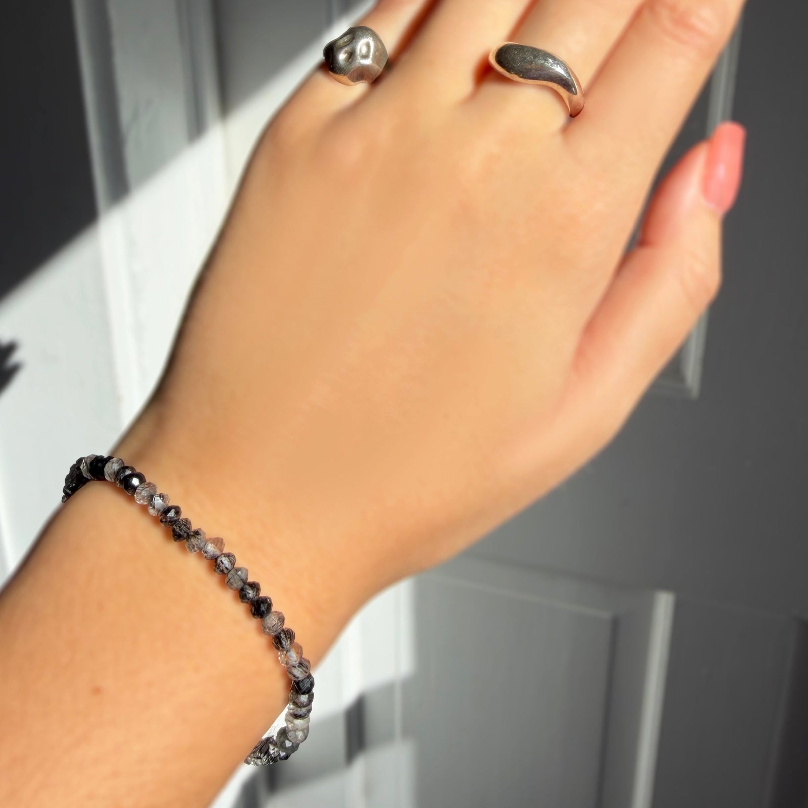 A  model wearing a faceted rutilated quartz beaded bracelet from AMANDA PEARL along with a recycled sterling silver molten skull pinky ring and molten ring.