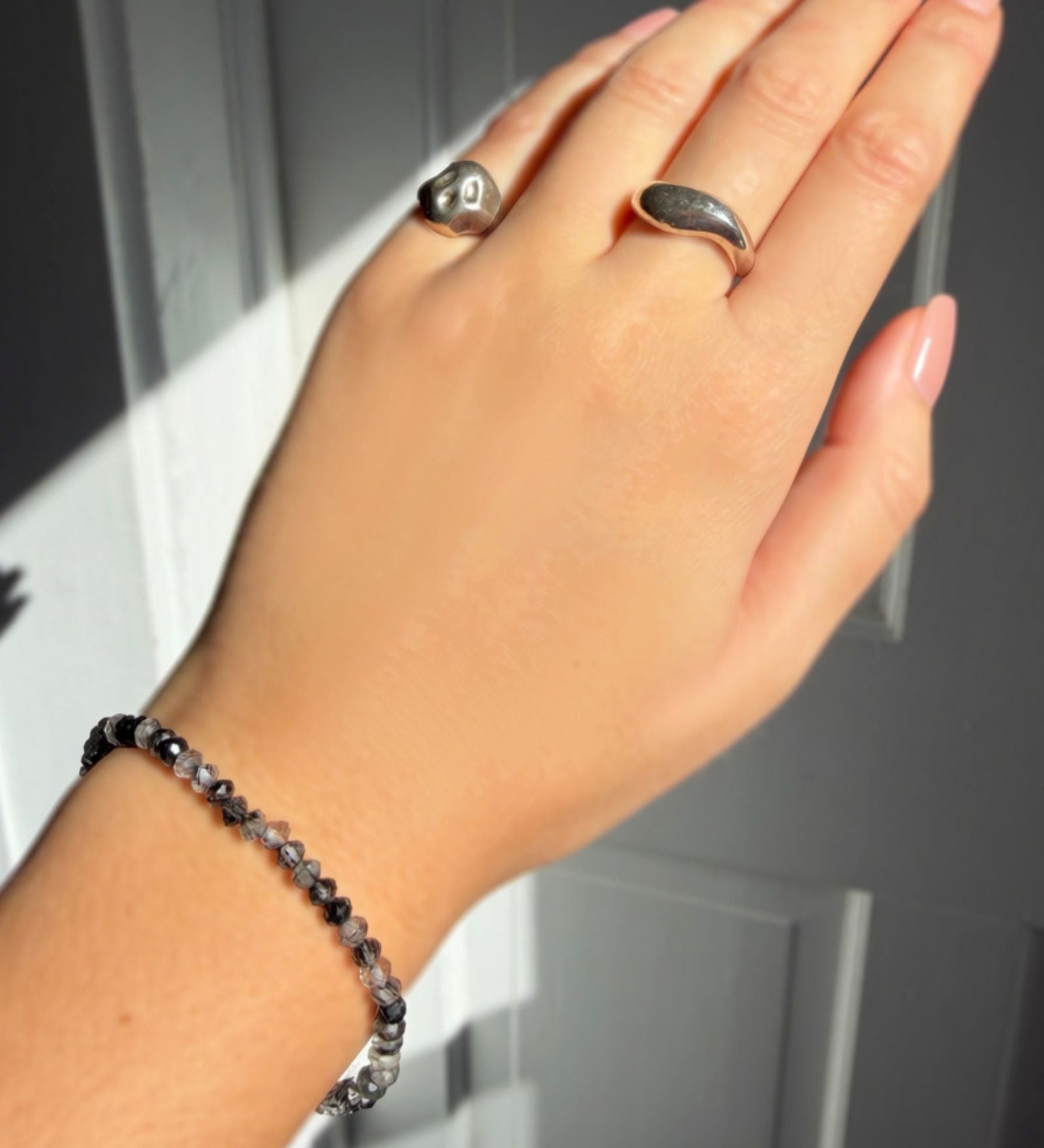 A  model wearing a faceted rutilated quartz beaded bracelet from AMANDA PEARL along with a recycled sterling silver molten skull pinky ring and molten ring.