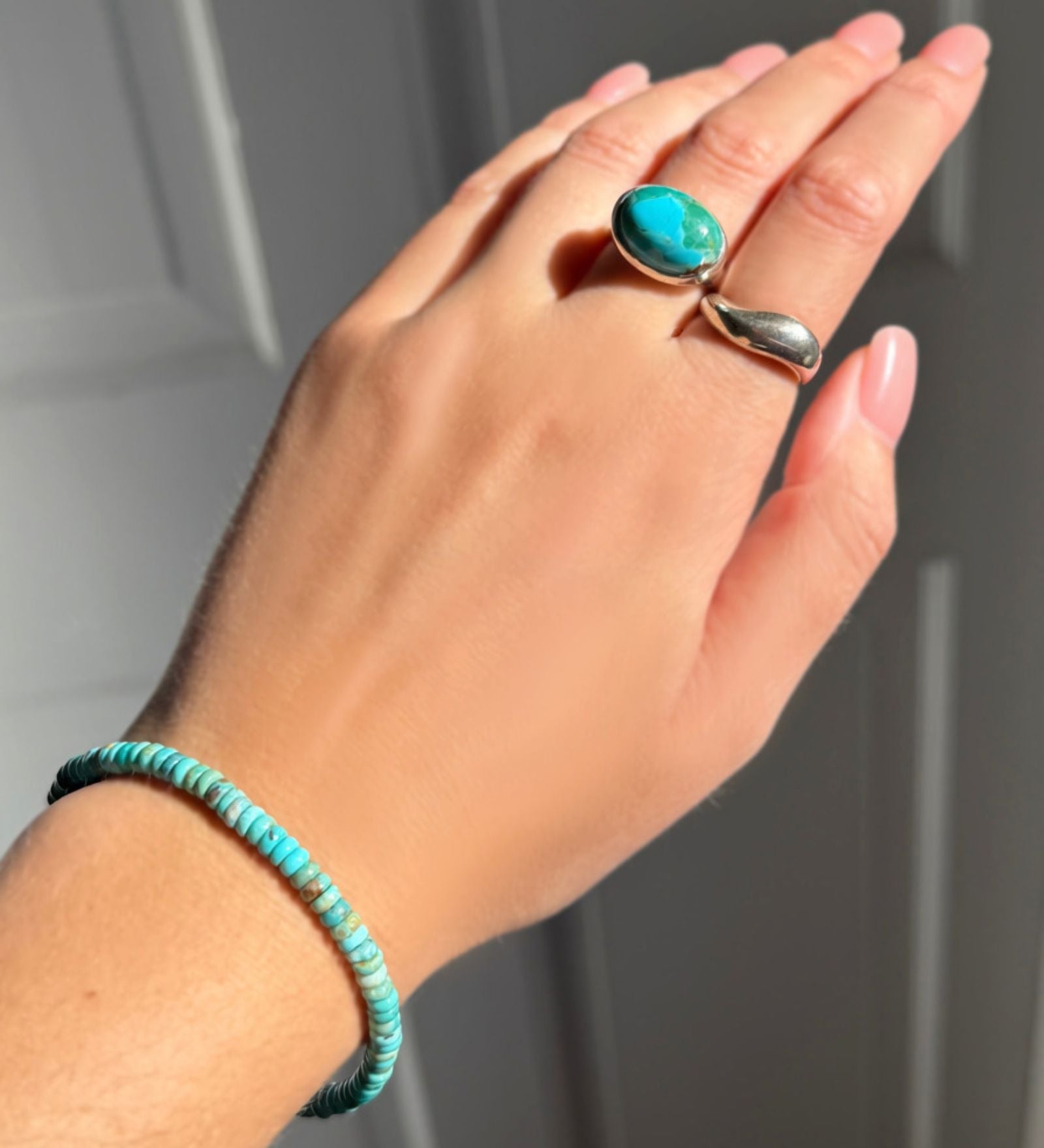 A model wearing an AMANDA PEARL turquoise rondelle bracelet, recycled sterling silver pebble ring with turquoise cabochon, and molten ring.