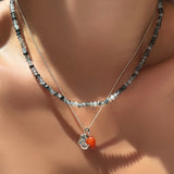 AMANDA PEARL sterling silver and faceted rutilated quartz necklace layered over a diamond cut bead chain with molten skull charm and carnelian drop charm on a model's neck.