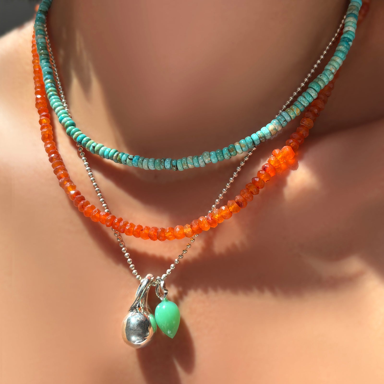 AMANDA PEARL sterling silver and turquoise rondelle necklace layered over a faceted carnelian necklace and bead chain with molten drop charm and chrysoprase drop charm on a model's neck.