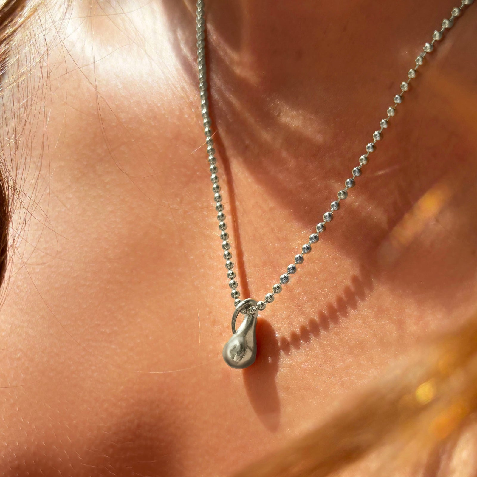 AMANDA PEARL recycled sterling silver mini molten drop charm on bead chain on a model's neck.