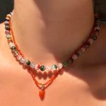 A Phantom Quartz Necklace on carnelian thread layered over a slim faceted carnelian necklace with carnelian drop charm on a model's neck.
