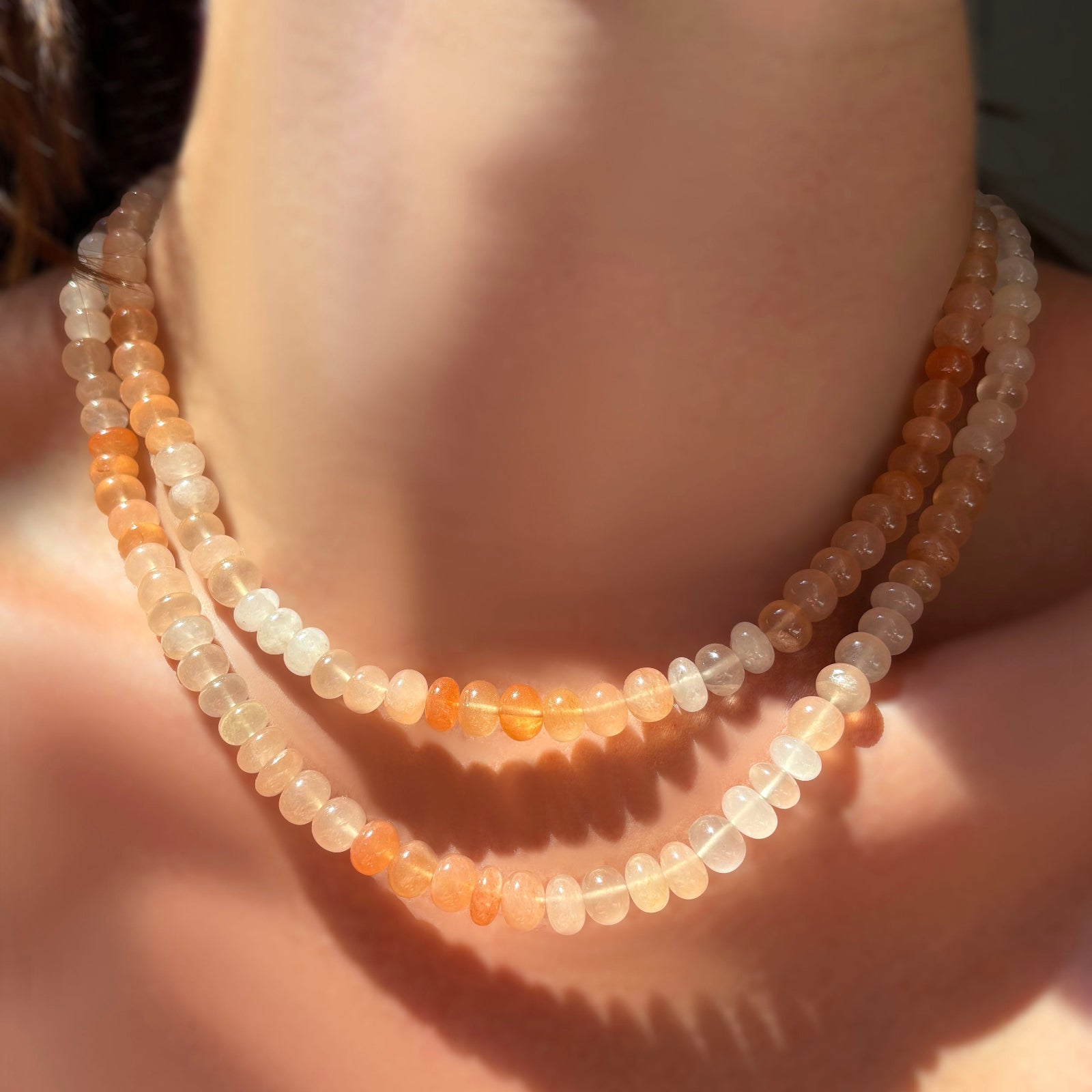 Two strands of ombré peachy strawberry quartz rondelle necklaces layered on a model's neck.