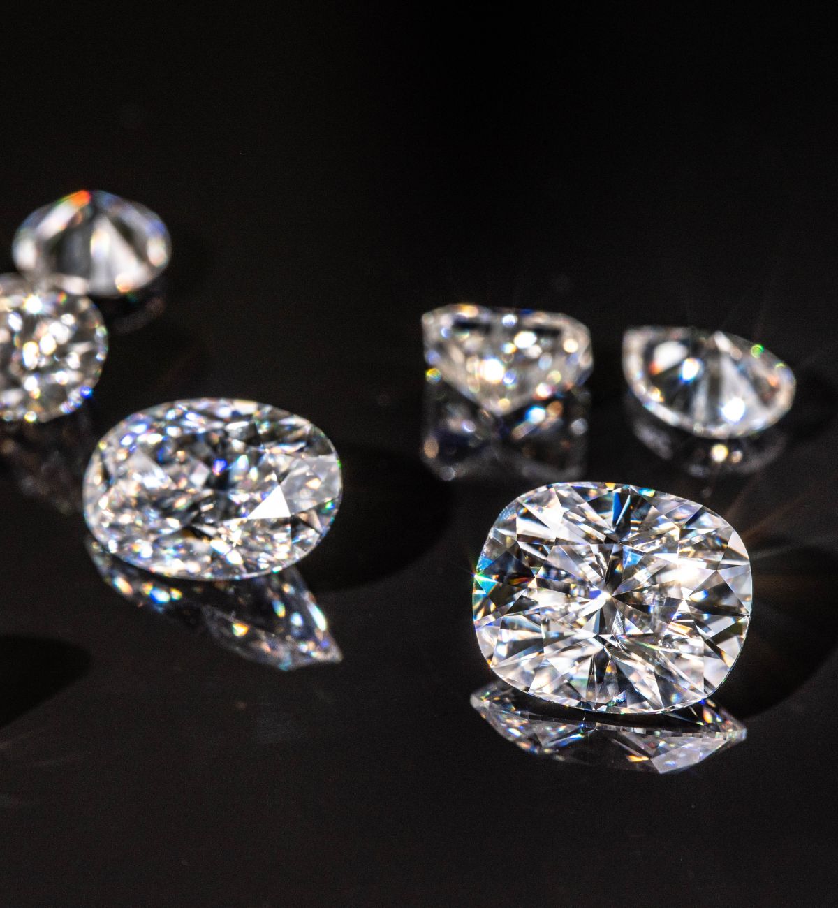 Faceted lab grown ethical diamonds of various shapes shine on a black background.