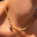 Solar yellow faceted sapphire necklace with a diamond pavé charm lock holding a rutilated quartz drop charm on a model's neck.