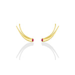 A pair of 14k recycled yellow gold climber earrings with a quill spike shape and a bezel set round ruby on a white background