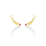 A pair of 14k recycled yellow gold climber earrings with a quill spike shape and a bezel set round ruby on a white background
