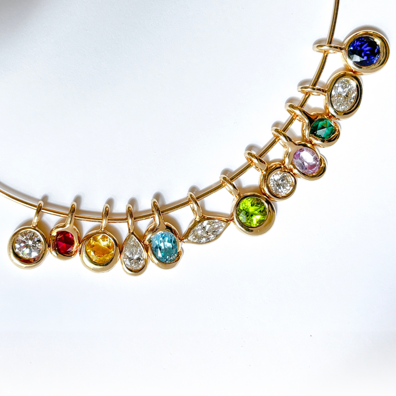 AMANDA PEARL Wire choker with an assortment of molten solitaire charms with diamonds and colored gemstones on a white background framed by shadows.